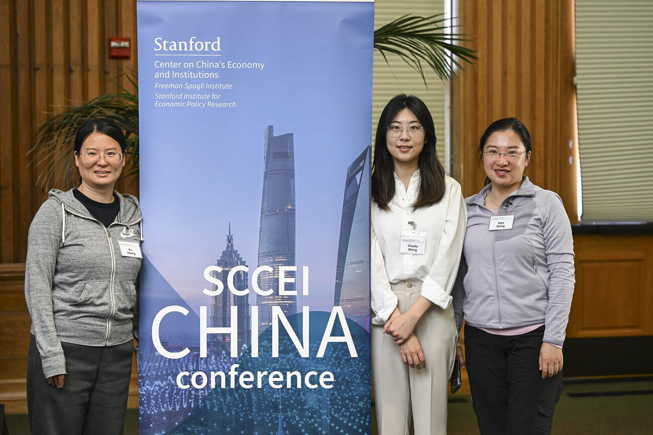 Three young women stand with the SCCEI China Conference banner.