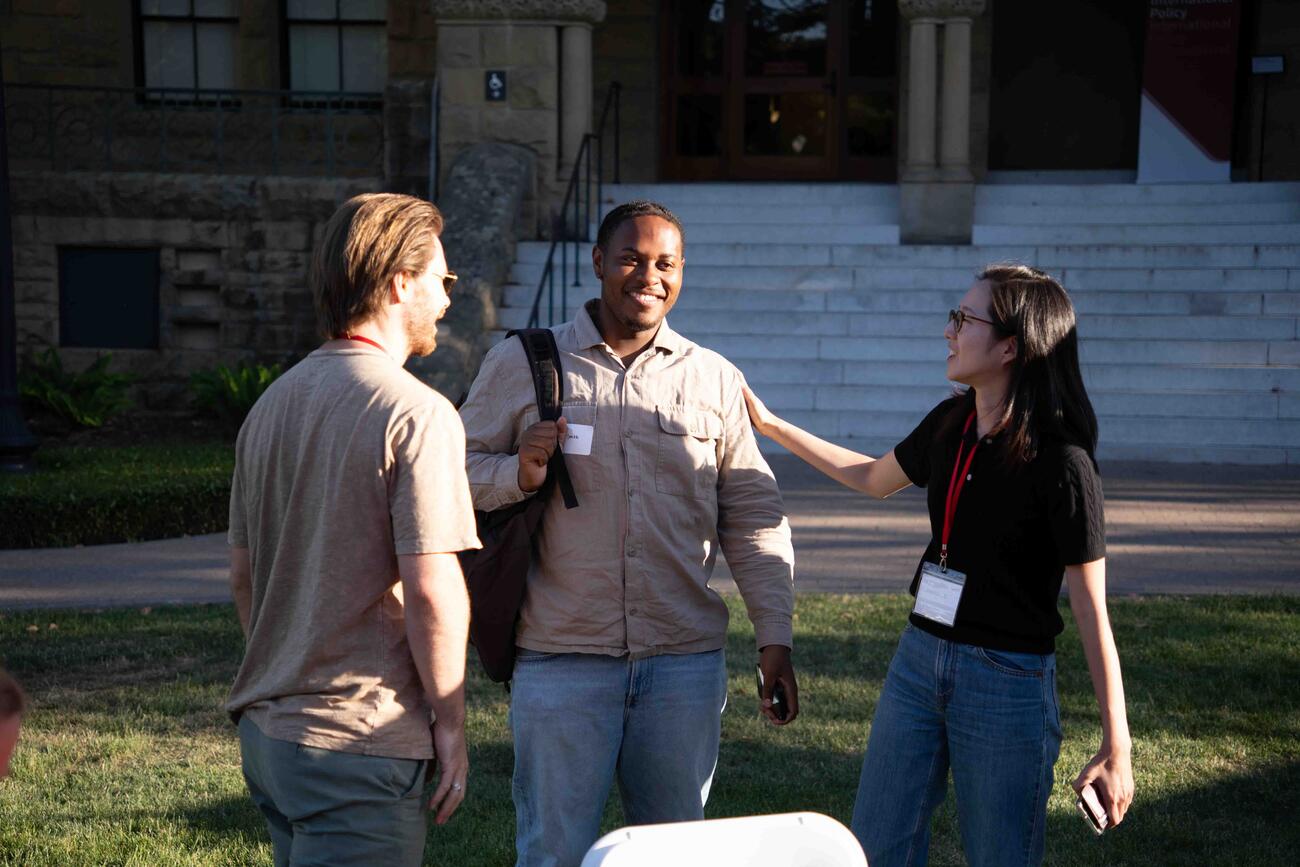 Three alumni of the Ford Dorsey Master's in International Policy chat near the steps of Encina Hall at Stanford University.