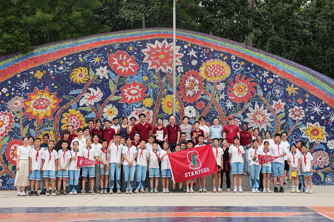 Photo of school kids and university students in front of a mosaic wall.