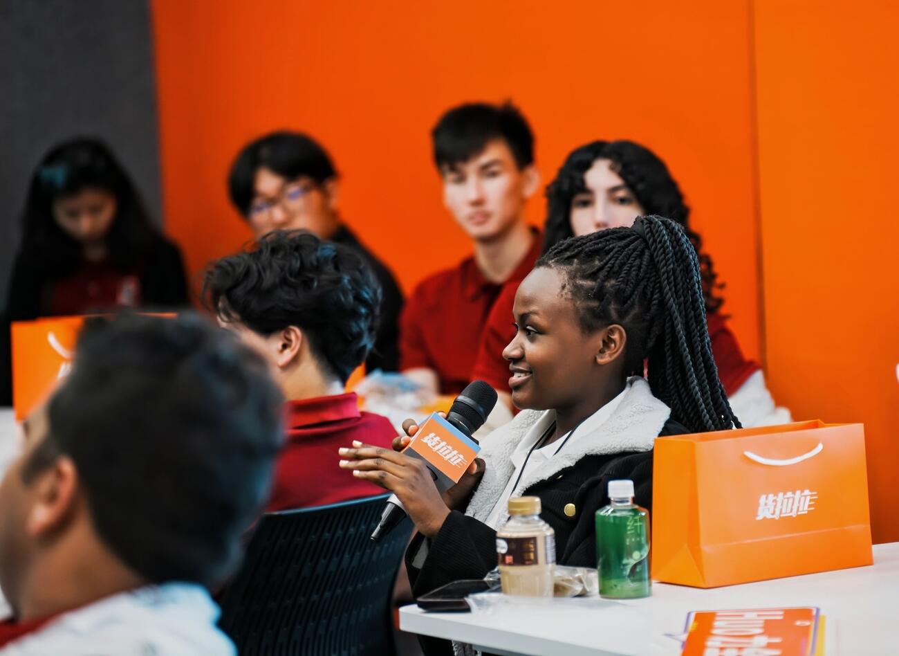 Student speaks into a microphone in an orange conference room.
