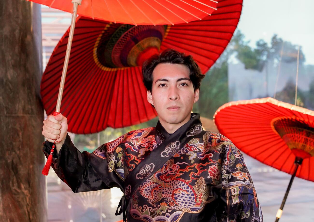 A young man poses in traditional Chinese attire and holds a paper umbrella.