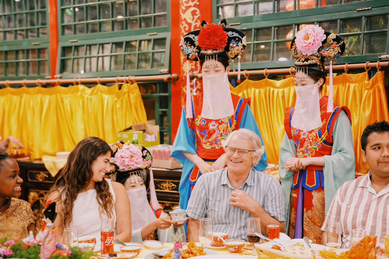 Scott Rozelle and students eat in a colorful restaurant in China with a woman dressed as a geisha behind.