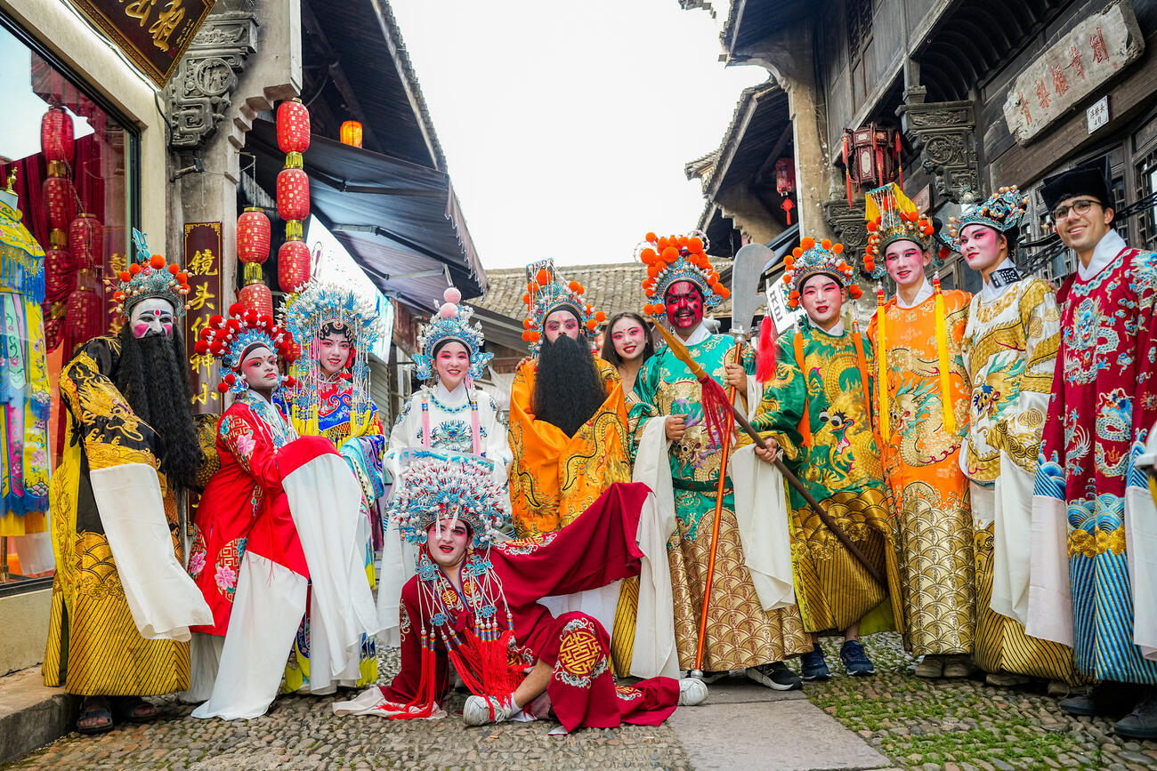 A group of students dressed up in Chinese opera attire and face paint pose together.