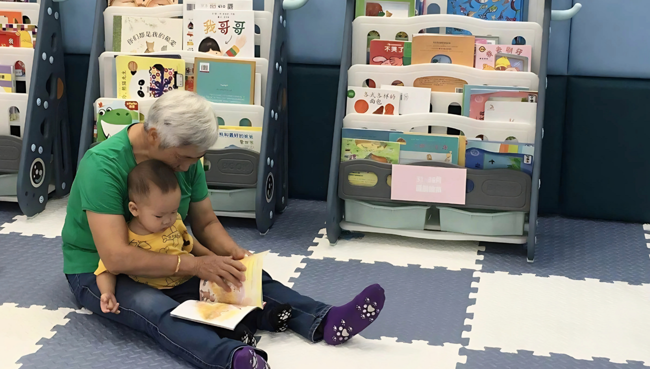 A grandparent holds a child in their lap and reads to them.