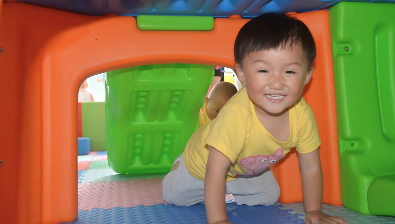 A toddler crawls through a colorful play structure. 