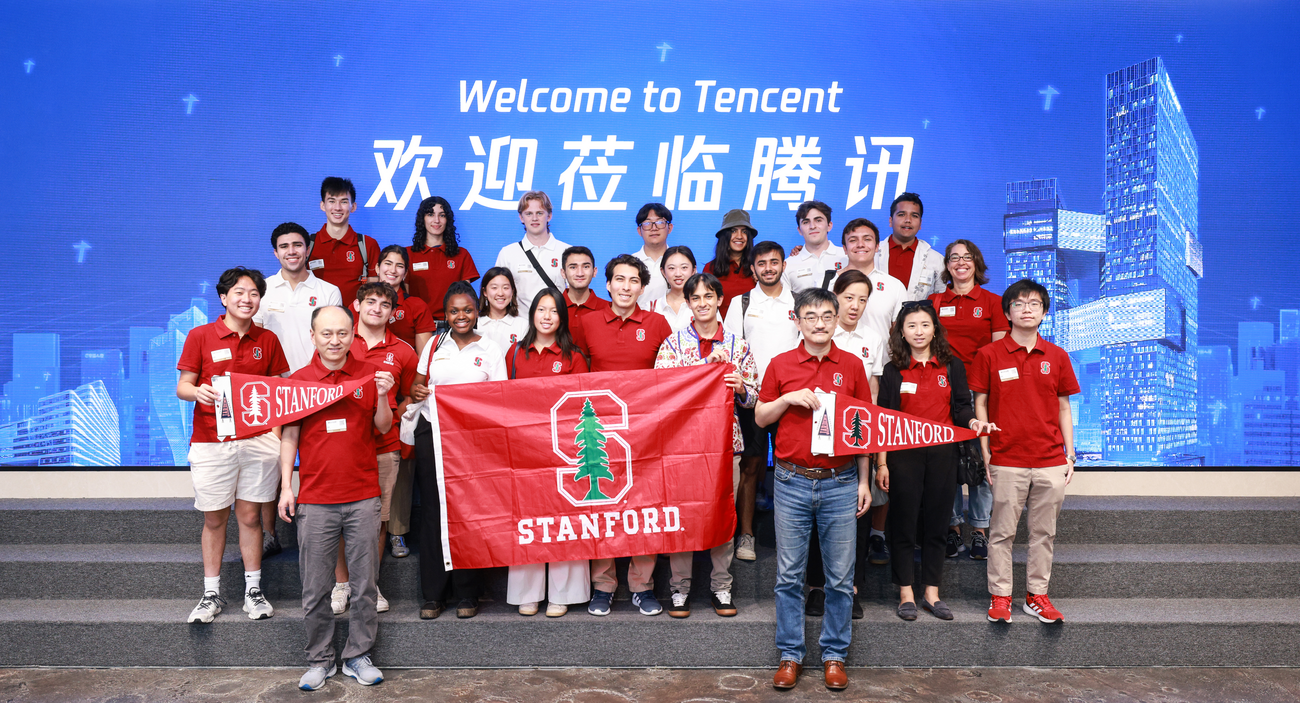 Group photo of students, staff, and faculty in China with Stanford flag at Tencent.. 