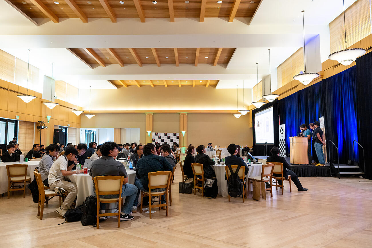 Participants at the 2025 Sushi Hackathon seated around tables in a conference room.