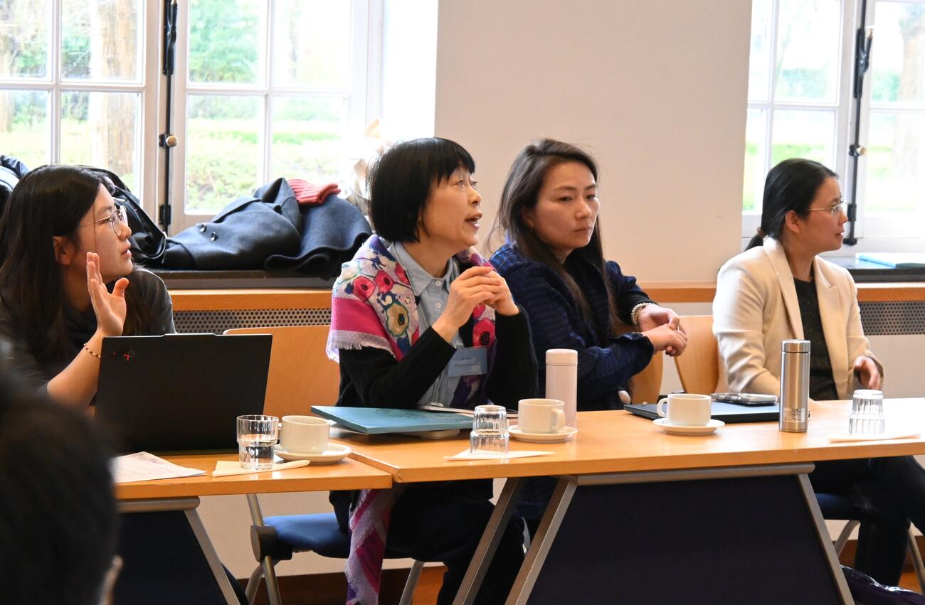 Women sit at a table and engage in conversation during a conference session.