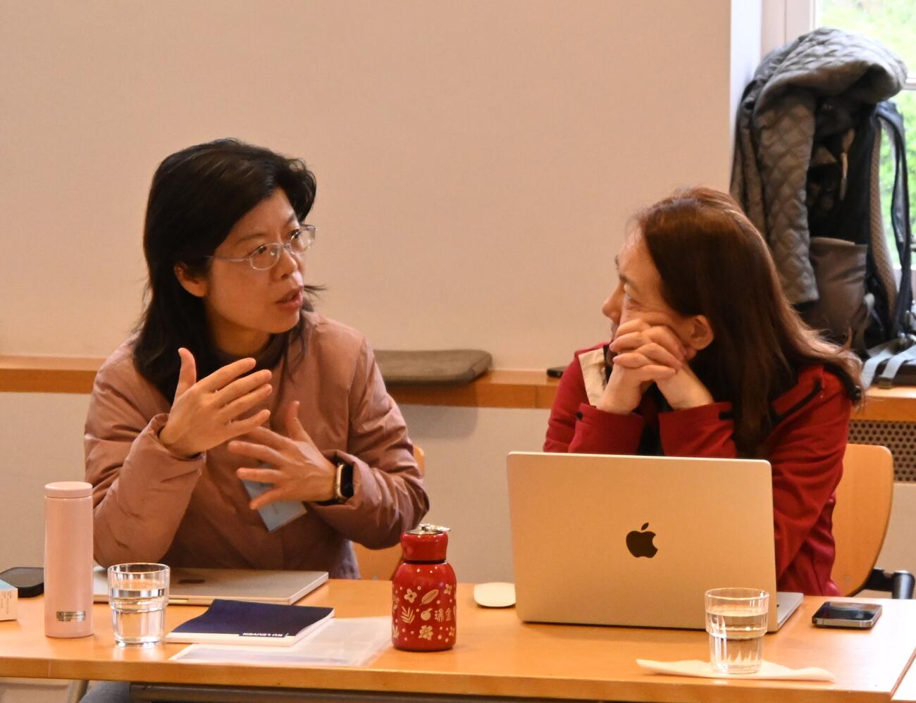 Women sit at a table and engage in conversation during a conference session.