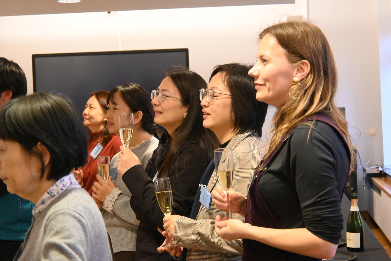 People stand with champagne glasses listening to a speech at a reception.