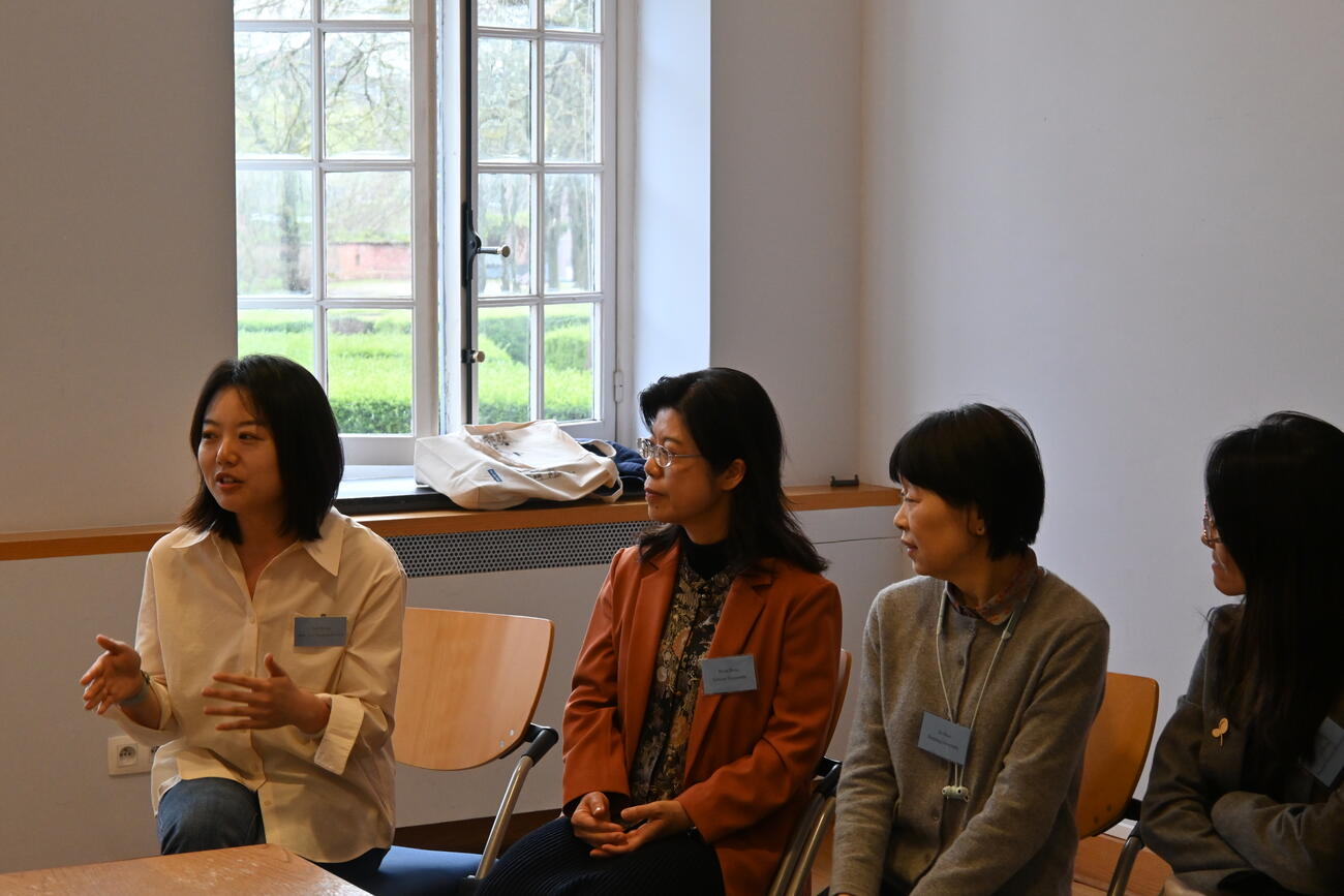 Women sit at a table and engage in conversation during a conference session.