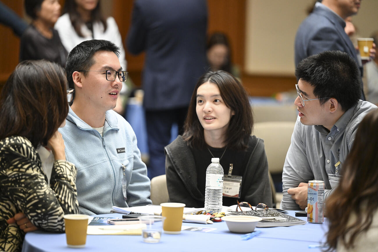 Students sit at a table and talk during a conference break.