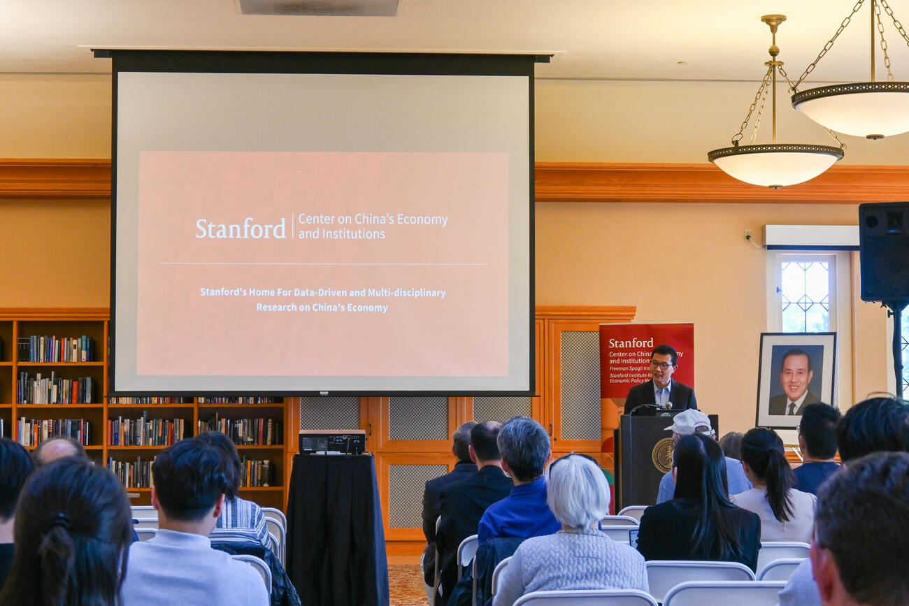 Yiqing Xu speaks at the front of a lecture room and seated audience.