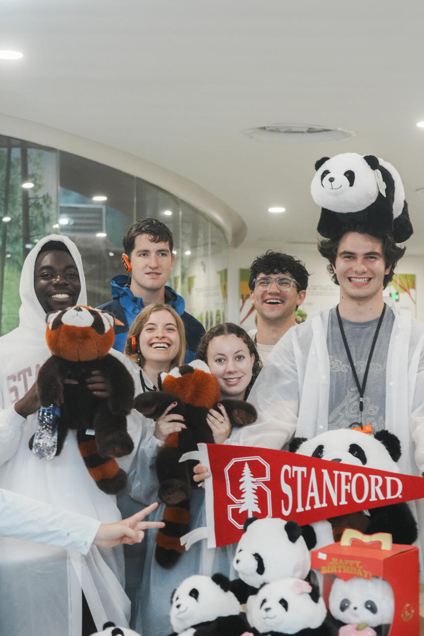Students pose with stuffed pandas and a Stanford flag.