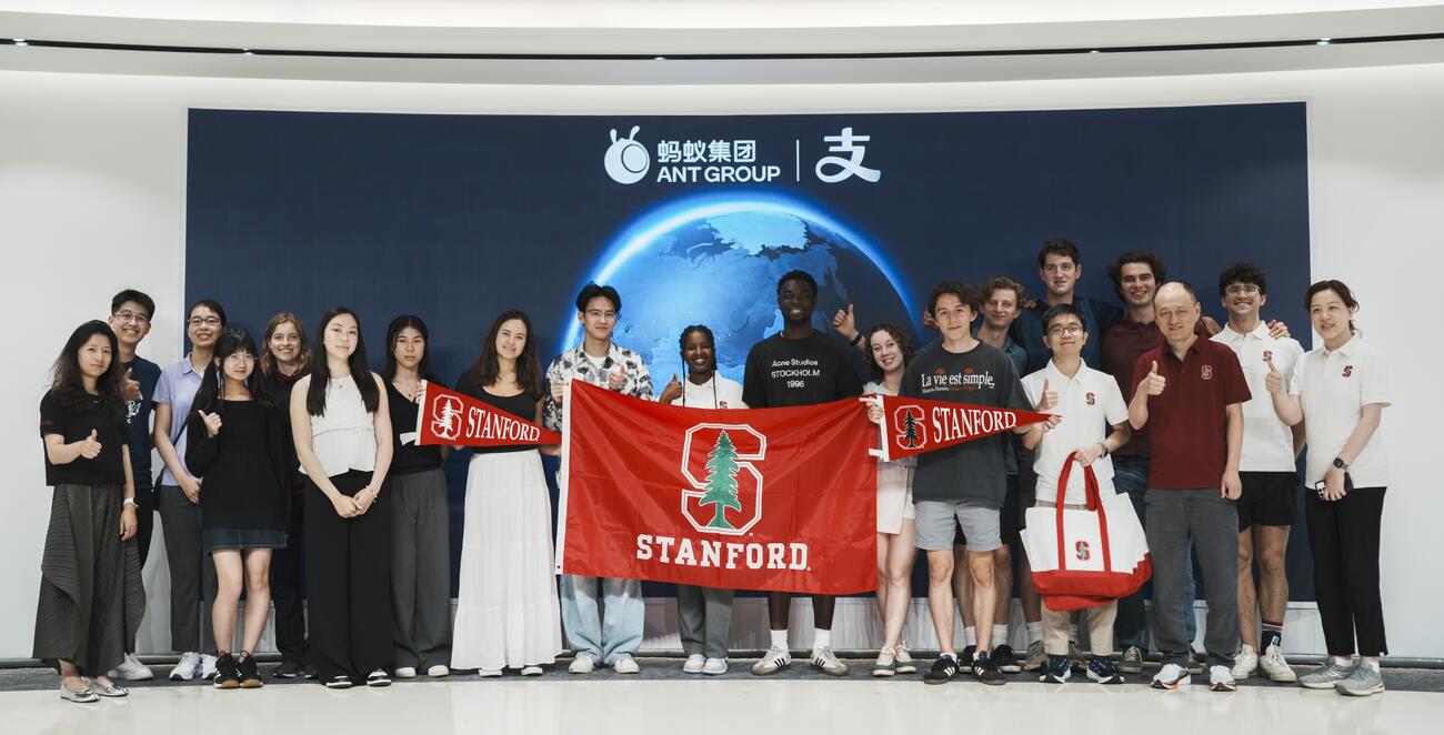 A group of students stand with a Stanford flag.