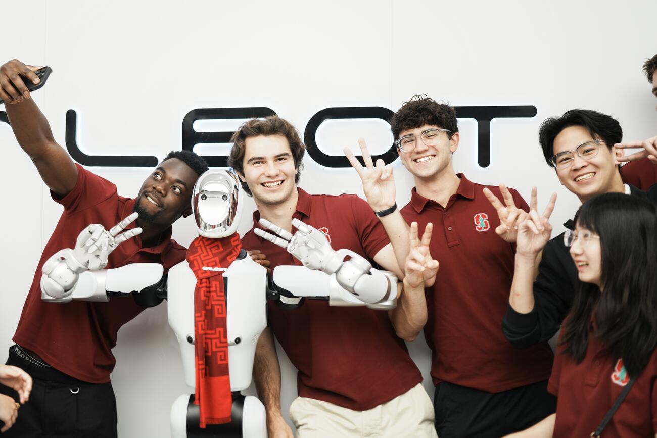 Students pose with a robot giving a peace sign.