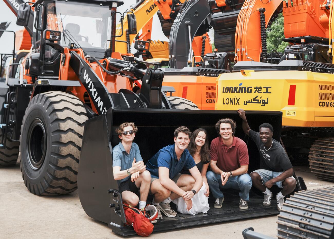 Students sit inside bulldozer shovel.