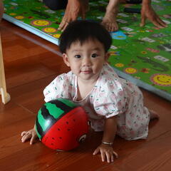 Baby crawls on floor with a ball colored as a watermelon. 