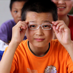 Boy holds new glasses to his face.