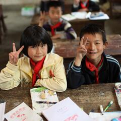 Young school kids smile and pose with peace signs in a rural classroom in China.