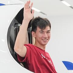 Ryan sits in a model plan and waves inside a white show room.