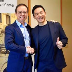 Two men smiling and shaking hands standinf in a conference room.