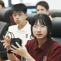 Lilian speaks into a microphone at a conference table with other students.