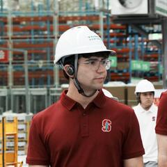 A student stands on a factory floor with a hardhat on