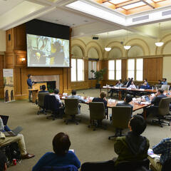 People seated in a conference room watching a speaker at a podium and a presentation on a screen.