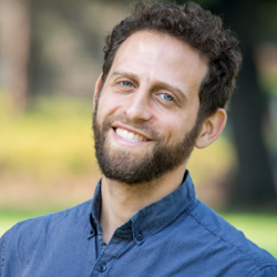 Izzy Gainsburg smiling at the camera, wearing a blue collared shirt