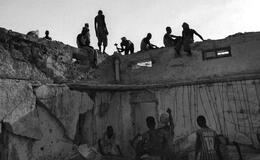 groups of people sitting on and standing near a dilapidated wall