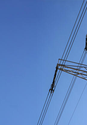 Looking up steel power pylon construction with high voltage cables against blue sky