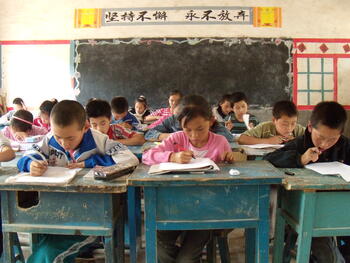 Middle school kids work at desks in a run down classroom in rural China.