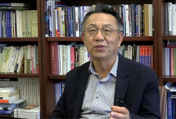 Gi-Wook Shin seated in his office, speaking to the camera during an interview.