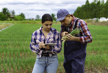 Two farmers discuss a crop issue; one is referring to a digital tablet.