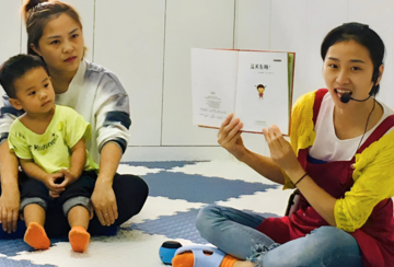 A staff member at a parenting center reads a book aloud to a child and caregiver.
