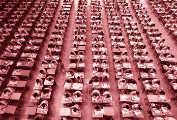 Hundreds of students sit at desks in rows taking an exam.