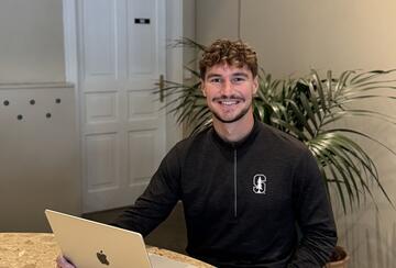 Photo of MIP student Nik White sitting in front of a laptop and smiling