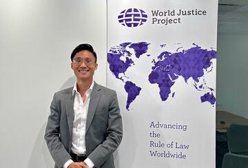 MIP student Haolie Jiang posing in front of a World Justice Project banner