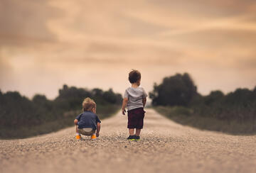 Two toddlers walking down a dirt road