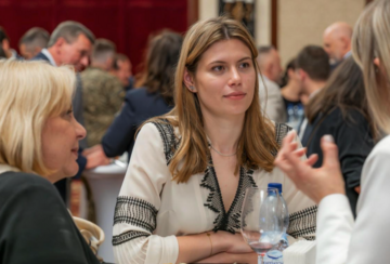 Image of MIP Student Sophia Yushchenko sitting at a table in a crowded room, engaged in conversation