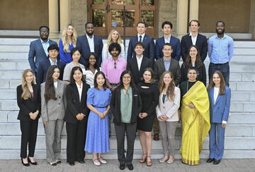 The class of 2027 of MIP students standing on the steps in front of Encina Hall at Stanford University.