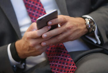 Close-up of a person in a suit and red patterned tie using a smartphone, with a wristwatch visible on their left wrist.