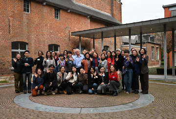 A group of conference attendees pose in a courtyard raising hand signs that indication 0 to 3.