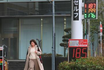 A woman walks past signs displaying gasoline prices outside a gas station on March 13, 2026, in Kobe, Japan. 