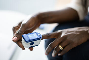 Photo of a dark-skinned woman using a pulse oximeter