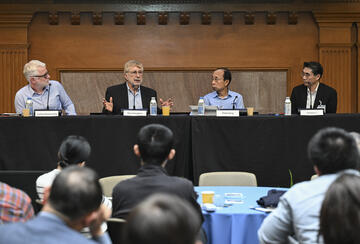 A panel of men sit at a long table on a stage.
