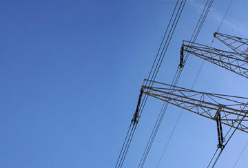 Looking up steel power pylon construction with high voltage cables against blue sky