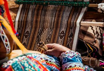 Woman working on a loom wearing traditional dress in Peru.