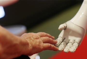 Elderly woman's hand touching a robot's hand. Photo from a summit on AI's potential for empowering humanity.